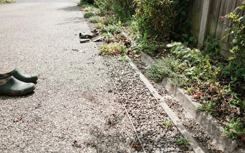 A permeable gravel driveway with a stone border directing water away from the house